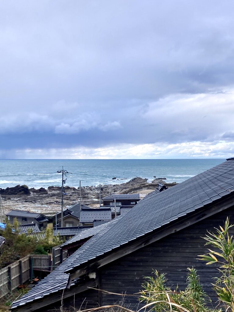 光沢のある黒い能登瓦の屋根が並ぶ集落とその背後に広がる日本海の風景